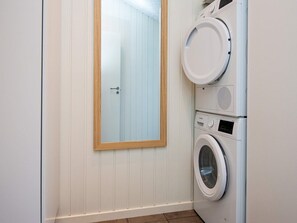 A laundry room with a washing machine and dryer stacked on top of each other, a wooden-framed mirror on the wall, and a door with a handle. - 5 Star Holiday Home in Sydals (Sydals)