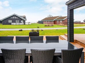 An outdoor dining area with a table and chairs, a wooden deck, and houses in the background. - 5 Star Holiday Home in Sydals (Sydals)