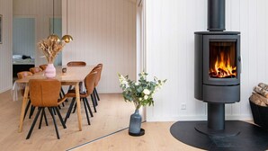 A modern interior with a central dining table, chairs, a vase with dried plants, a blue vase with flowers, and a wood-burning stove. - 5 Star Holiday Home in Sydals (Sydals)