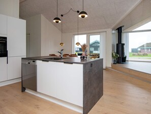 A modern kitchen with a central island, built-in dishwasher, pendant lighting, and a view of the outdoors.
