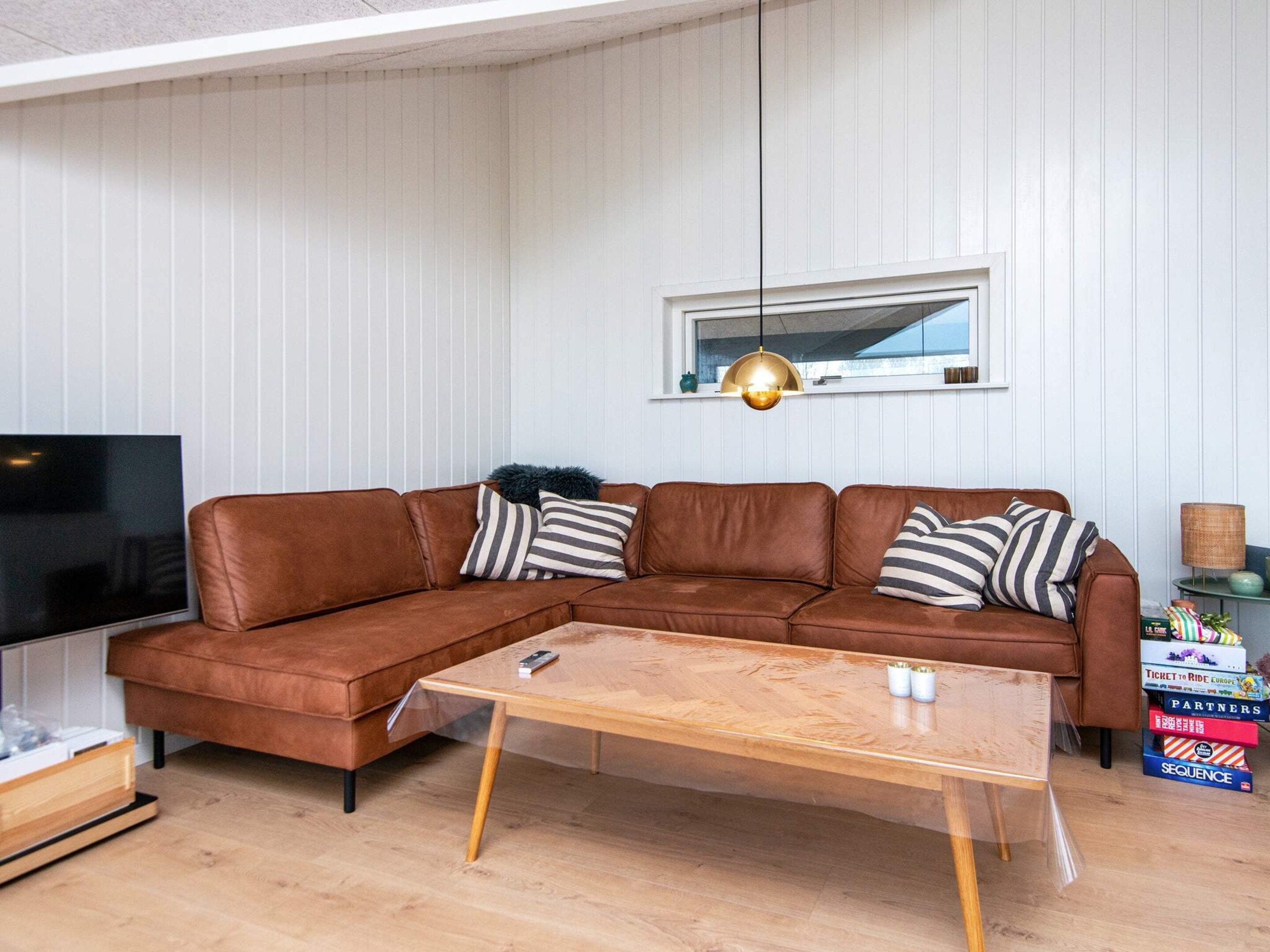 A modern living room with a brown leather sectional sofa, a wooden coffee table, a flat-screen TV, and a pendant light.