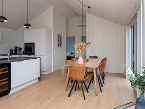 A modern kitchen with a central island, a dining area with a wooden table and chairs, and a large window providing natural light.
