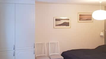 A bedroom with a bed, two chairs, a wardrobe, and two framed pictures on the wall.