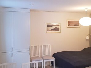 Una camera da letto con un letto, due sedie, un armadio e due quadri appesi al muro.