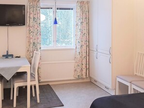 A room with a bed, a desk, a chair, a radiator, a window with curtains, and a television on the wall. - 4 Star Holiday Home in Ljusdal (Ljusdal)