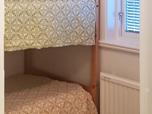 A bunk bed with a patterned bedspread and a window with blinds.