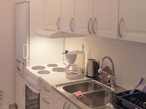 A compact kitchen with white cabinets, a stove, a coffee maker, a kettle, and a sink. - 4 Star Holiday Home in Ljusdal (Ljusdal)
