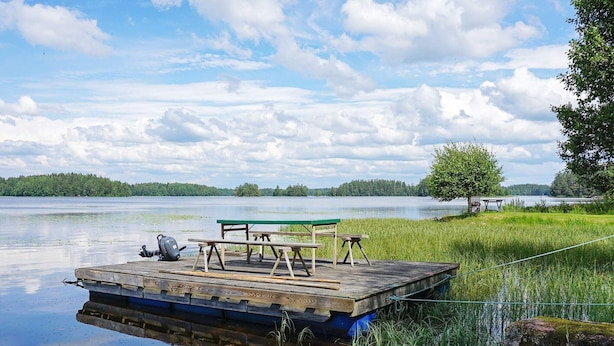 En træbrygge med picnicborde og en bænk, omgivet af stille vand og grønt.