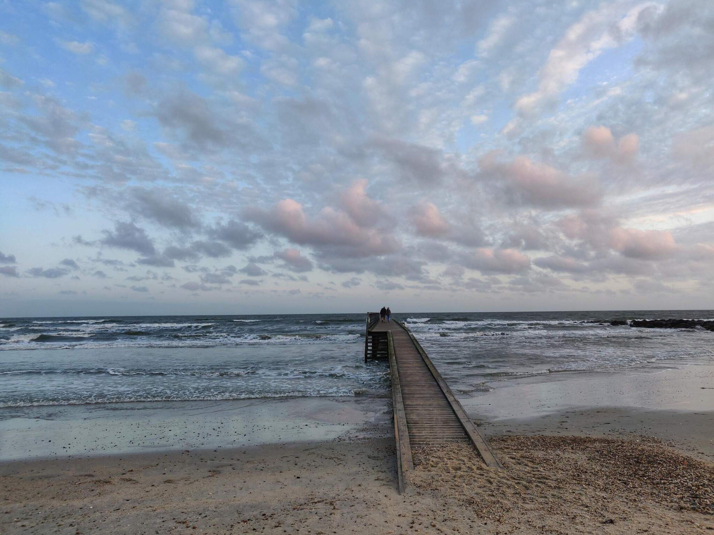 A wooden pier extending into the ocean with waves crashing at the end.