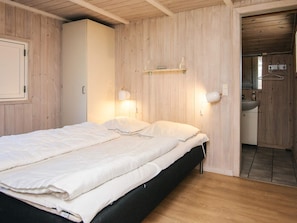 Une chambre à coucher avec un lit, des murs en bois, une armoire et une salle de bain visible à travers une porte ouverte.