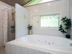 A bathroom with a white bathtub, a shower, a window with a view, and a potted plant. - 4 Star Holiday Home in Blavand (Blavand)
