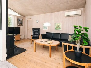 Uma sala de estar moderna com piso de madeira, um sofá de couro preto, uma mesa de centro de madeira, uma poltrona de couro preto, uma televisão e um vaso com planta.