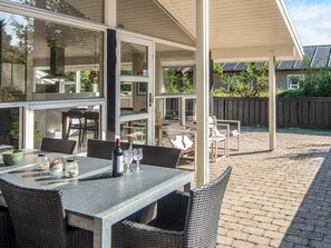 Pátio externo com mesa posta para refeição, cadeiras de vime e uma garrafa de vinho.