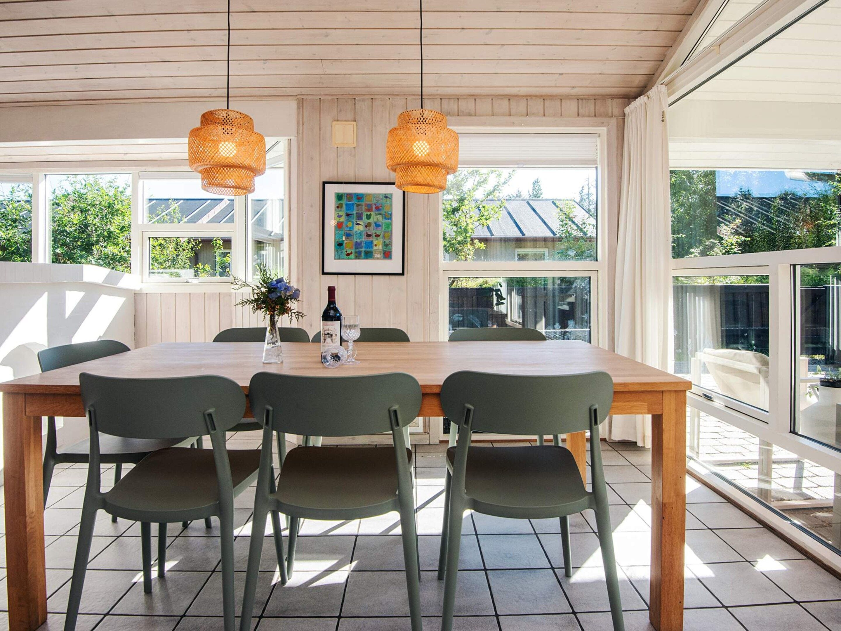 Un coin repas avec une table en bois et quatre chaises, deux lampes suspendues et un tableau encadré au mur.