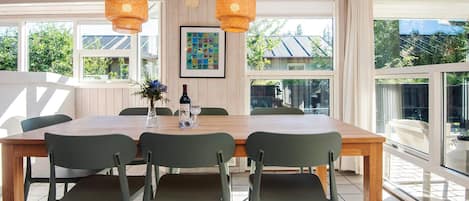 A dining area with a wooden table and four chairs, two hanging lights, and a framed picture on the wall.