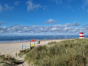 A beach with a red and white striped lighthouse, grassy dunes, and informational signs. - 4 Star Holiday Home in Blavand (Blavand)