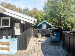 Un chalet en bois avec un chemin bordé de briques, un banc bleu et un petit abri de jardin, le tout situé dans une zone boisée.