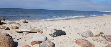 Una playa con grandes rocas y piedrecitas, una orilla arenosa y el océano al fondo.
