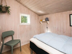 A room with a bed, a chair, a window, a shelf with a lamp, and a hanging plant. - 4 Star Holiday Home in Blavand (Blavand)