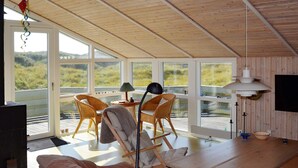 A spacious room with large windows, wicker furniture, a wooden table, and a ceiling fan. - 6 Person Holiday Home in Fano-by Traum (Fano)
