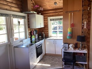 A compact kitchen with white cabinets, a stove, and a sink. There are windows allowing natural light, and a small shelf with kitchen items. - 6 Person Holiday Home in Hovborg (Hovborg)