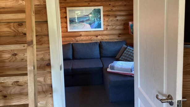 A cozy cabin interior with a wooden ceiling, a framed landscape painting, and a dark-colored sofa with cushions. - 6 Person Holiday Home in Hovborg (Hovborg)