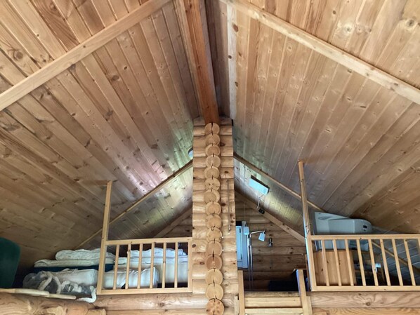 Une chambre mansardée en bois, avec un plafond en pente, des rampes en bois et un lit en mezzanine avec du linge de lit.
