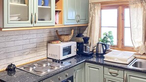 Eine Küche mit Mikrowelle, Kaffeemaschine und Toaster auf der Arbeitsfläche, einem Spülbecken und Schränken mit einem Fenster darüber.