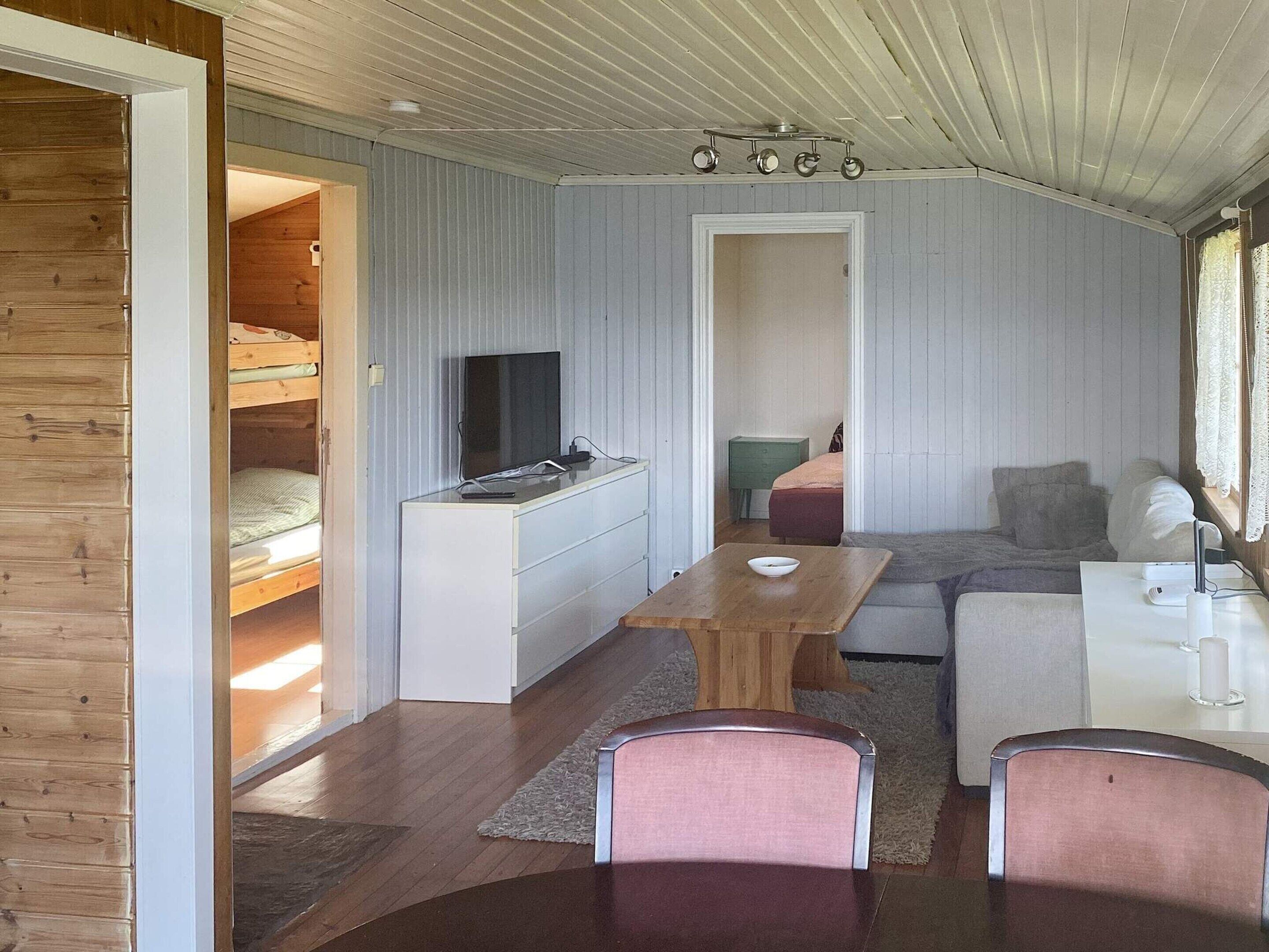 A compact, well-lit room with a bunk bed, a small kitchenette, a dining area, and a seating area with a sofa and chairs.