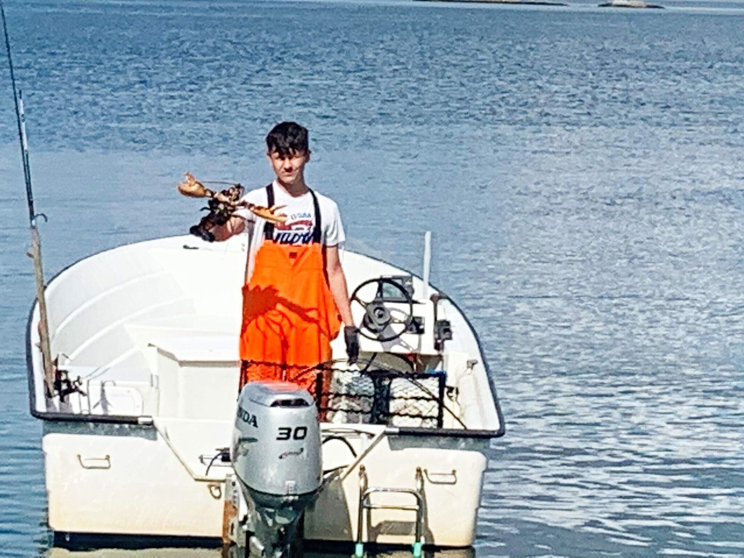 A person standing on a boat with a fishing rod, wearing an orange apron and a white shirt.
