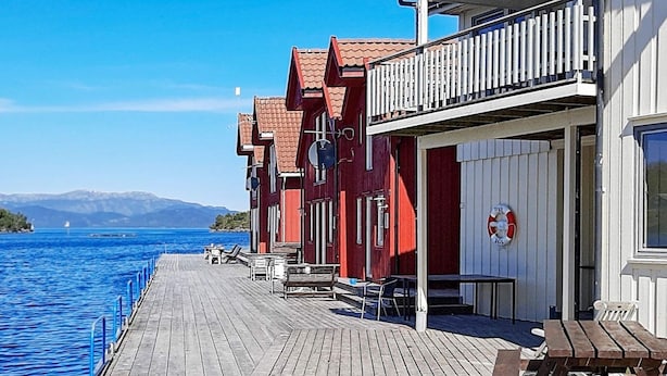 Une jetée en bois s’étendant dans une étendue d’eau, bordée d’une rangée de bâtiments rouges dotés de terrasses et d’une bouée de sauvetage fixée au mur.