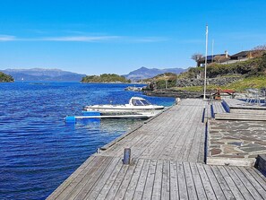 A wooden dock extending into a calm lake with a boat moored at the end. - 7 Person Holiday Home in Sjernaroy (Stavanger)