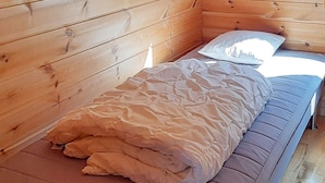 Un lit simple avec une couverture beige dans une chambre de cabane en bois.