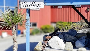 Une pancarte indiquant « Grillen » est fixée à un poteau bleu, avec un palmier et un mur de pierres en arrière-plan.