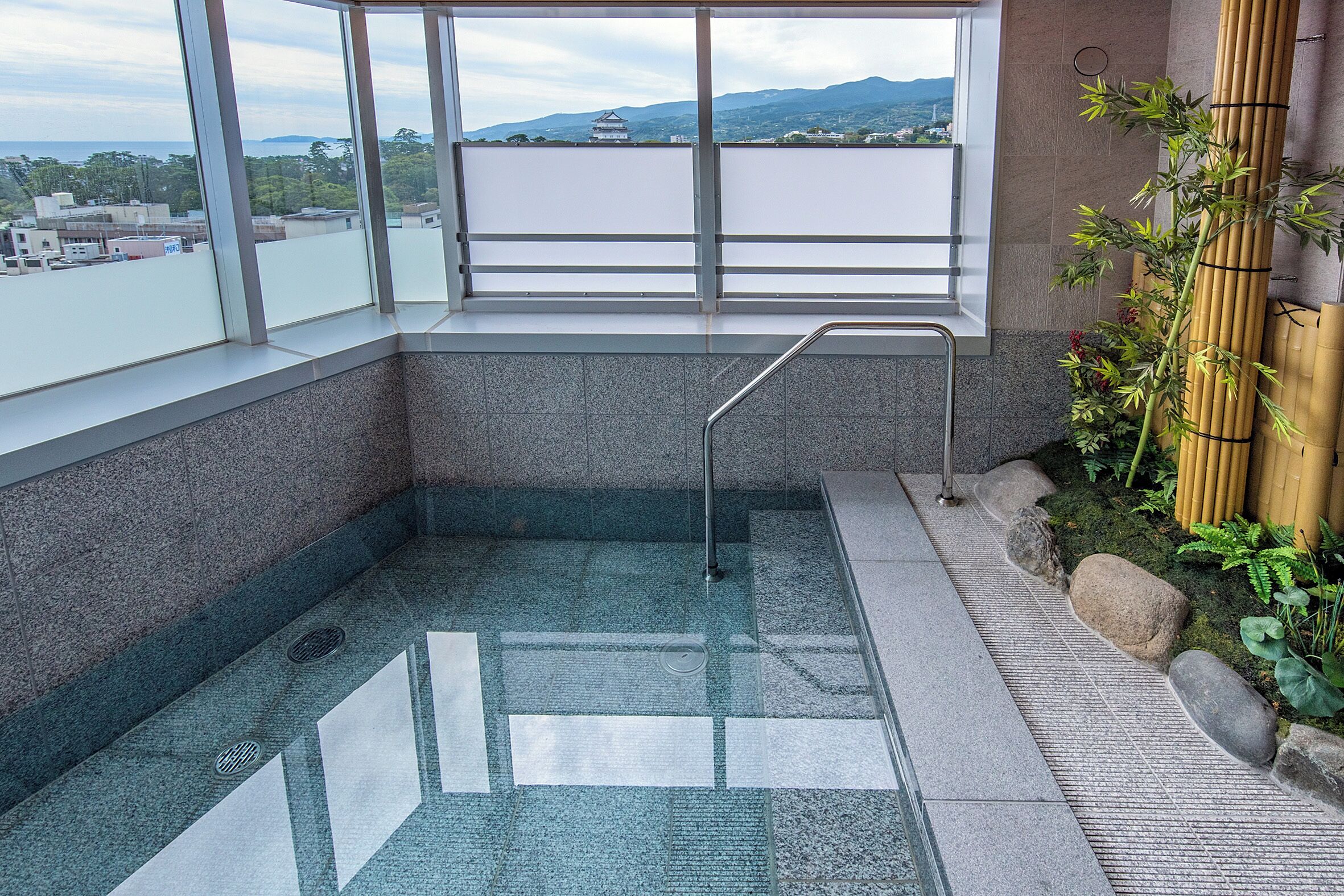 Un jacuzzi extérieur, entouré de parois en verre, offrant une vue sur les bâtiments et les montagnes au loin.