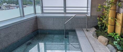 Un jacuzzi extérieur, entouré de parois en verre, offrant une vue sur les bâtiments et les montagnes au loin.
