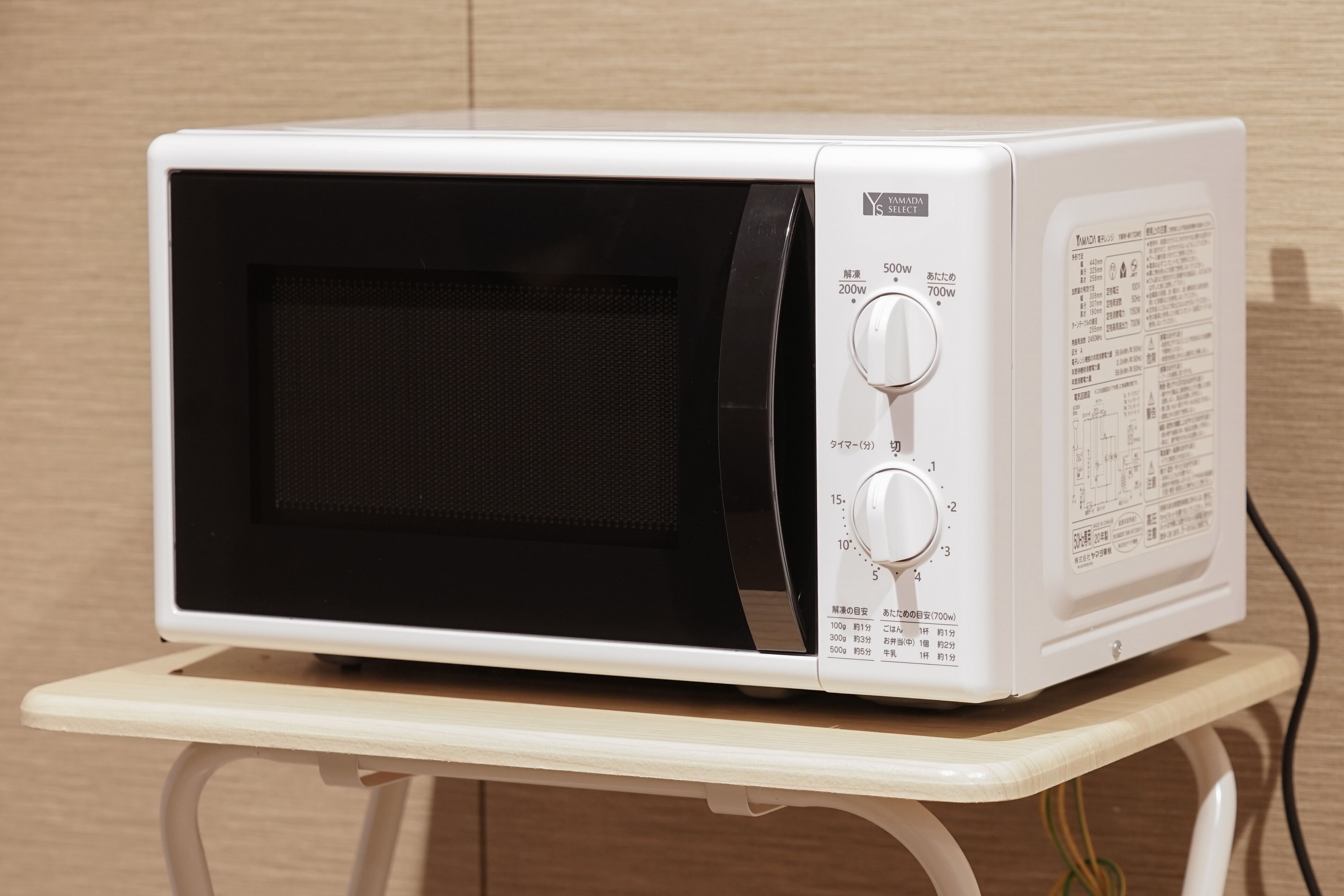 A white microwave on a small white table against a wooden wall.