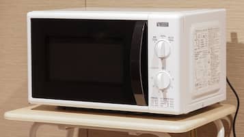 A white microwave on a small white table against a wooden wall.