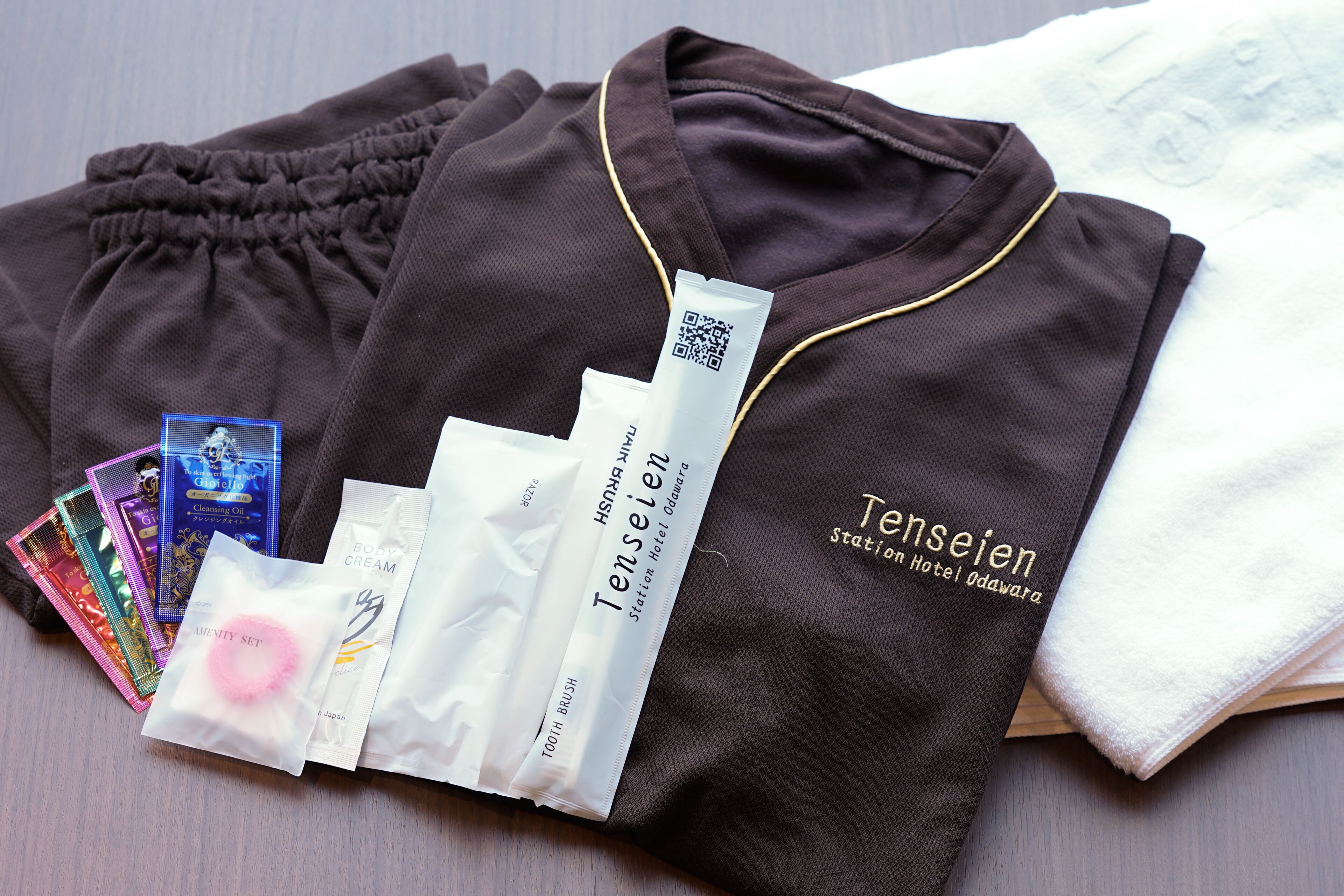 A neatly arranged set of toiletries including a toothbrush, body cream, and a hair care product, along with a branded towel and a brown robe.