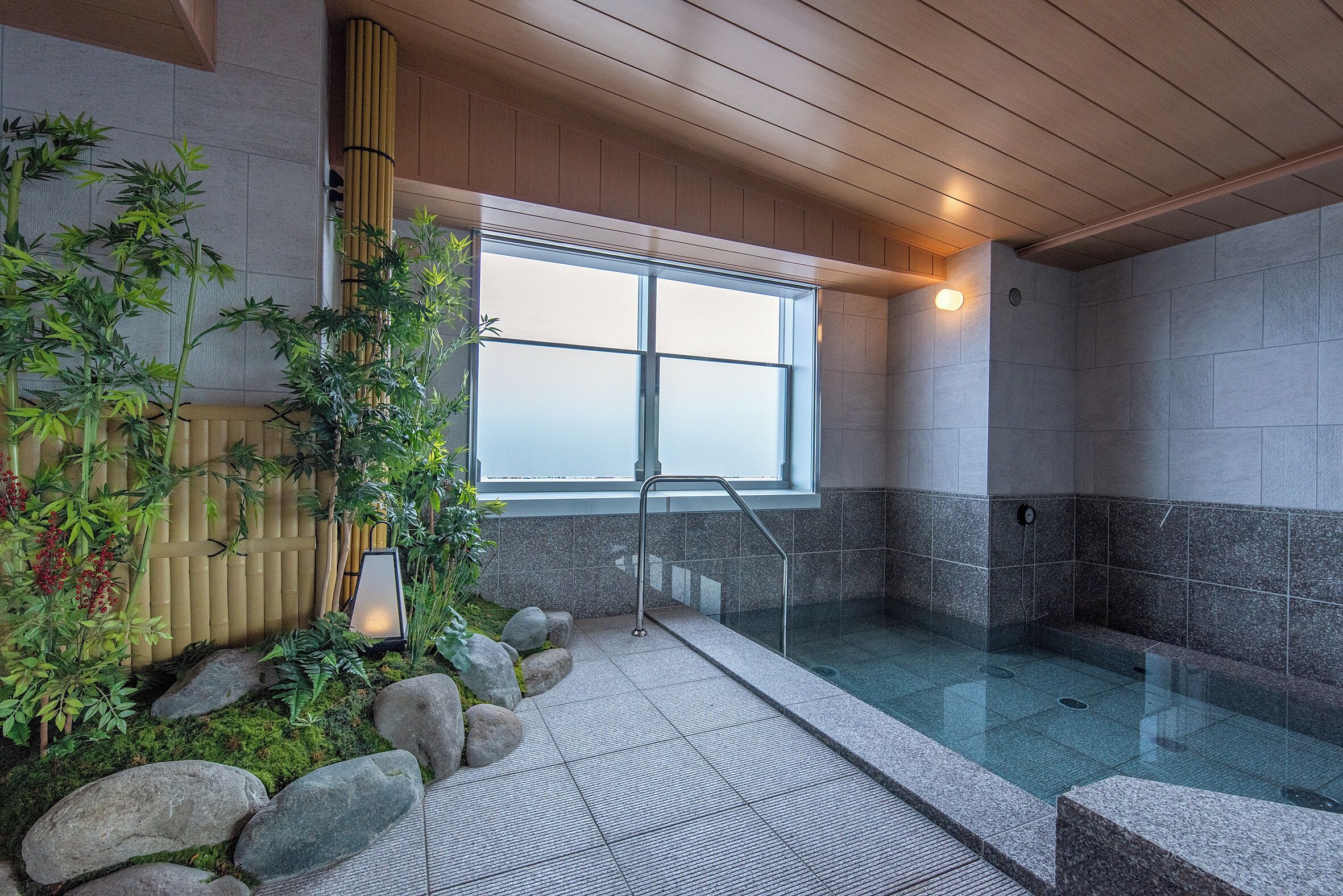 A modern indoor pool area with a glass barrier, bamboo plants, and a view through a large window.