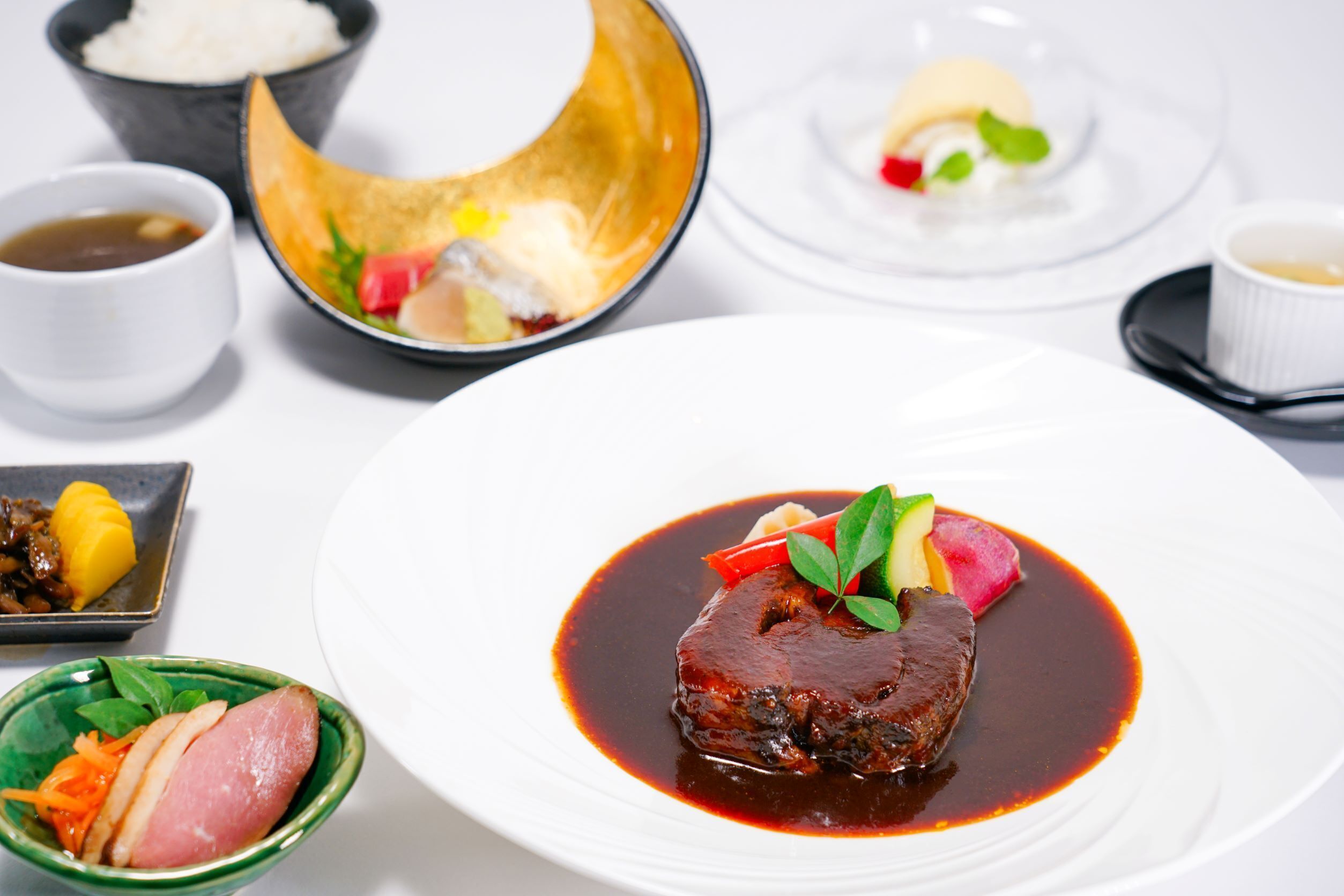 A variety of dishes on a table, including a prominent plate with a meat dish, a bowl of rice, and several small dishes with different sides.