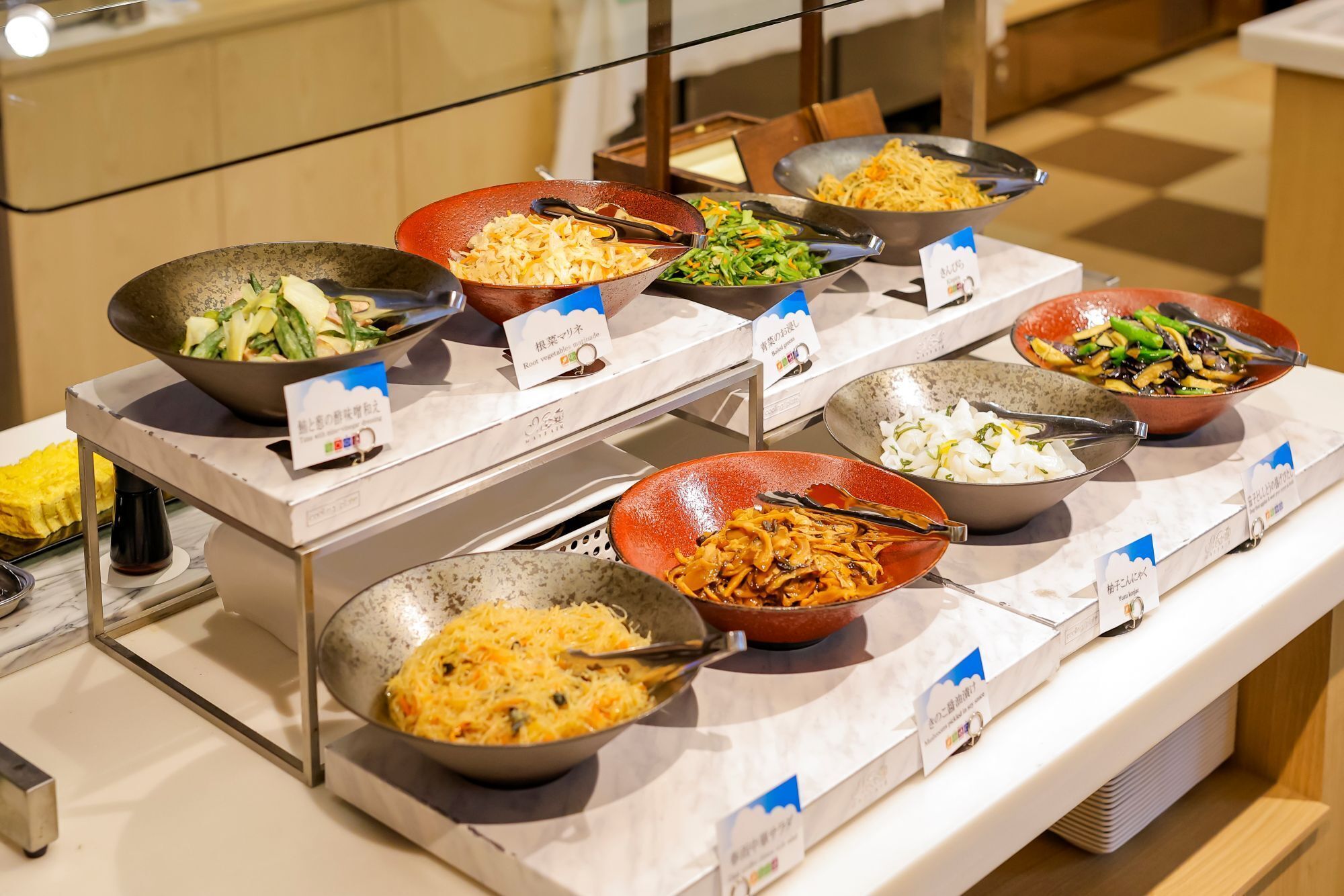 A buffet with various dishes in bowls, each labeled with a name and price tag.