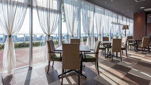 Ein Restaurant mit großen Fenstern, Innenbestuhlung und Blick auf die Stadt.