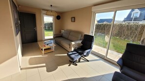 A living room with a sofa, a chair, a coffee table, and a large sliding glass door to the outside.