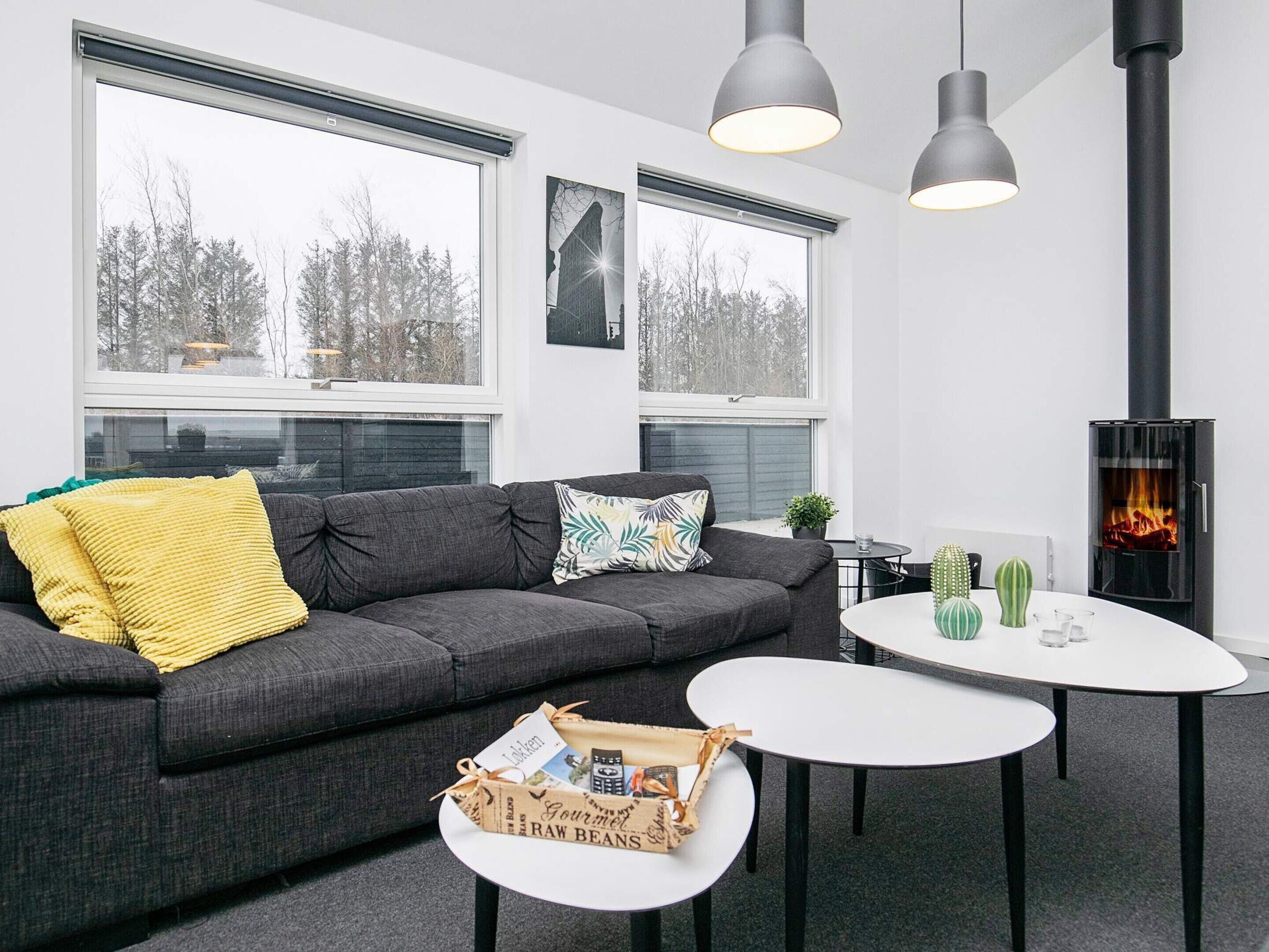 A modern living room with a sofa, two tables, a fireplace, and large windows.