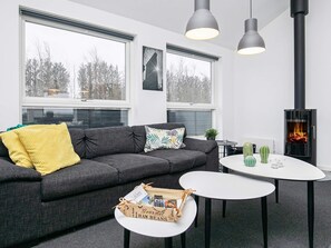 A modern living room with a sofa, two tables, a fireplace, and large windows. - 5 Star Holiday Home in Lokken (Lokken)