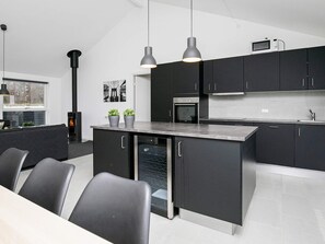 Une cuisine moderne avec des meubles de couleur sombre, un îlot central et des luminaires suspendus.