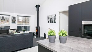 A modern kitchen with a built-in stove, dark cabinetry, and a dining area with a sofa and pendant lights.