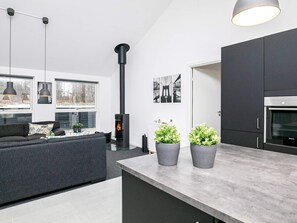 A modern kitchen with a built-in stove, dark cabinetry, and a dining area with a sofa and pendant lights. - 5 Star Holiday Home in Lokken (Lokken)