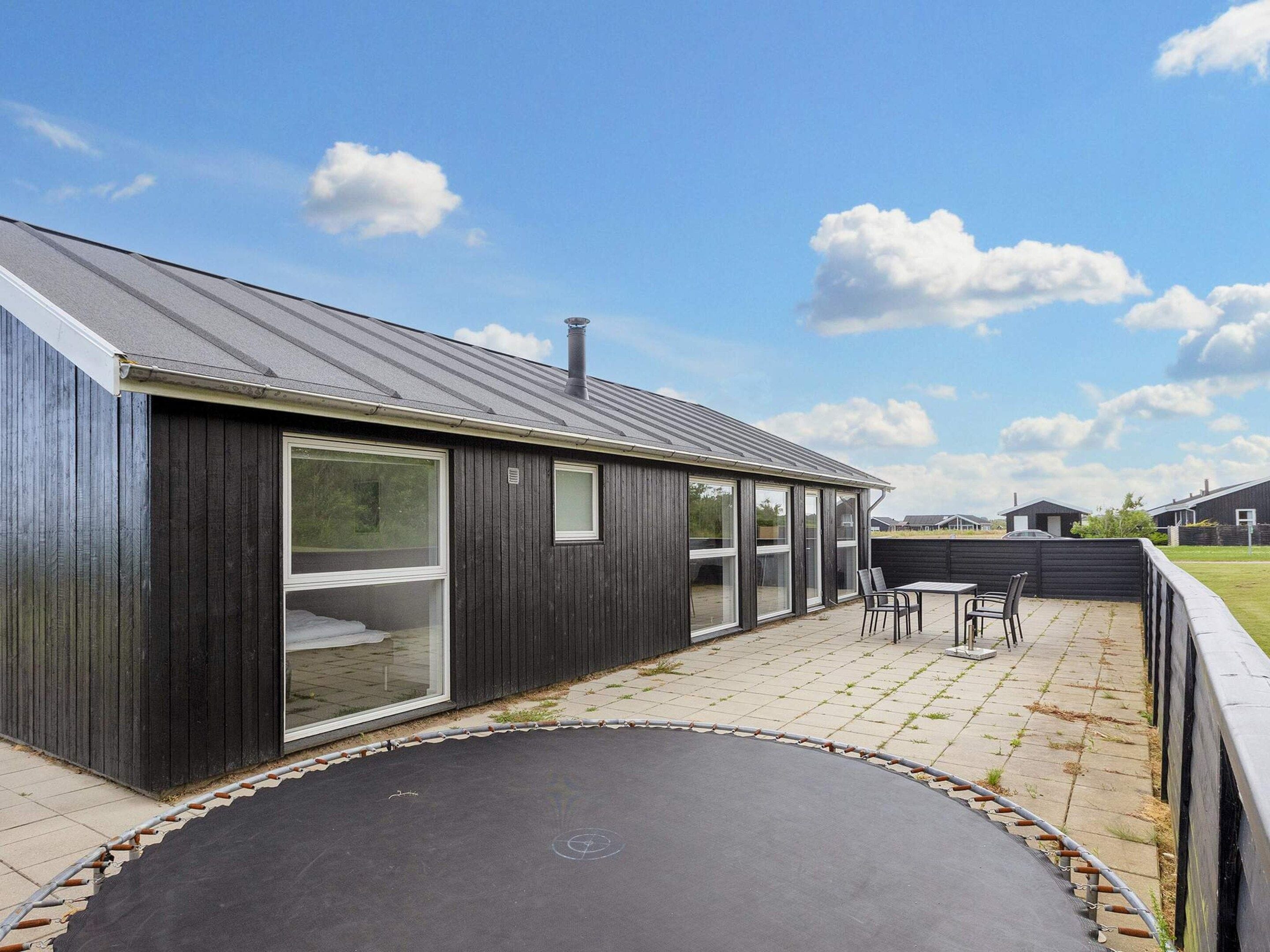 Un bâtiment moderne doté d’une grande porte-fenêtre coulissante, d’un patio avec un trampoline et d’un ciel dégagé.